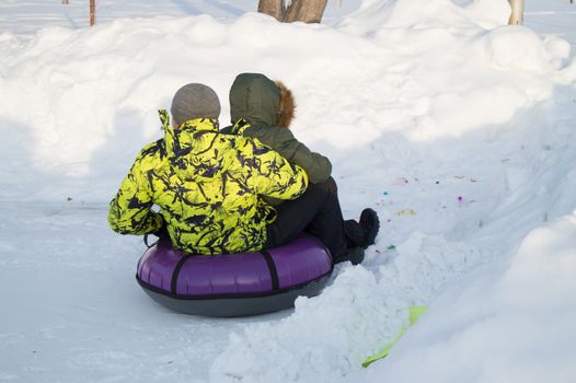 Winter entertainment. Two happy teenagers with pleasure ride on a tubing from the mountain. Sunny frosty day.