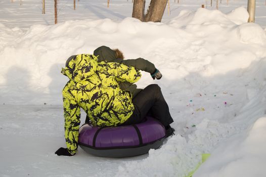 Winter entertainment. Two happy teenagers with pleasure ride on a tubing from the mountain. Sunny frosty day.