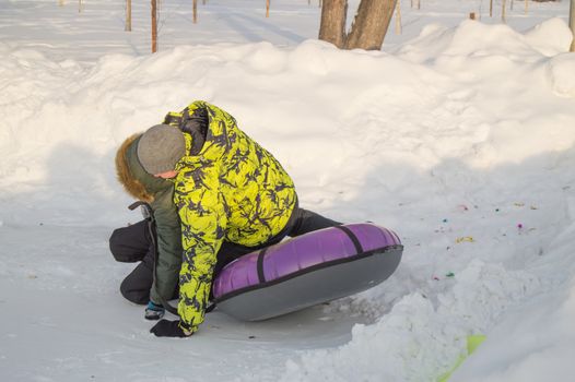 Winter entertainment. Two happy teenagers with pleasure ride on a tubing from the mountain. Sunny frosty day.