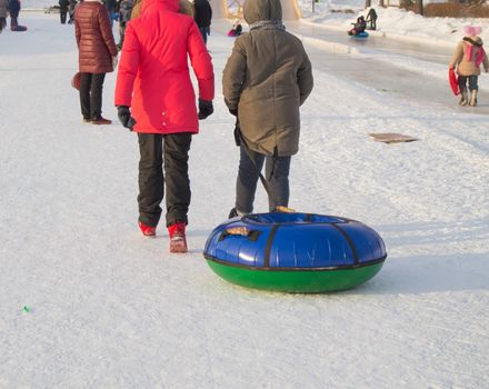 Two teen girls pull tubing after after sliding down the slope of an ice slide, winter fun in the Park.