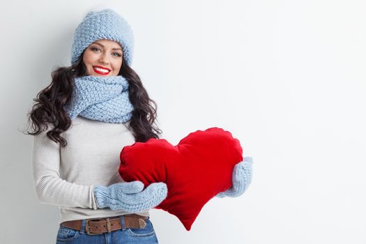 Beautiful woman in warm winter clothes with a big red heart shape pillow , copy space for text , Valentines day , love winter concept