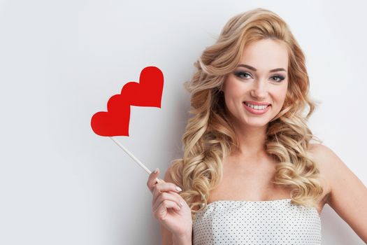 Portrait of funny positive girl with curly hair holds heart shaped glasses on stick and smiling