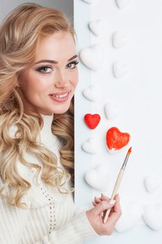 Beautiful young woman painting hearts with red paint
