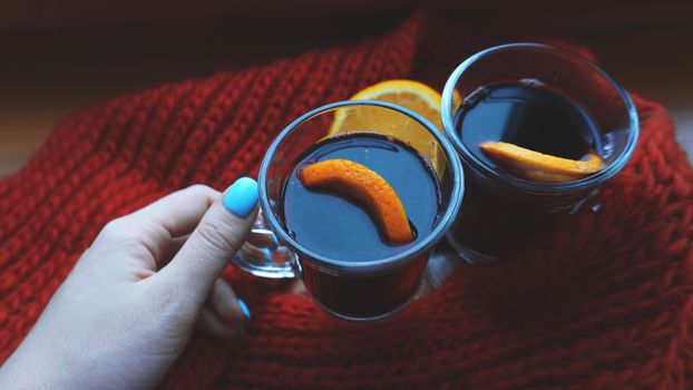 Woman holding mulled wine with spices and citrus fruit in her hand, close up Red Hot wine with orange and red scarf