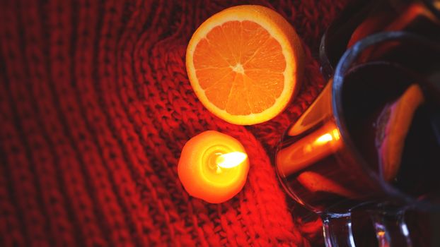 Mulled wine in glass mugs, burning candle on a dark red background. Red Hot wine with orange and red scarf