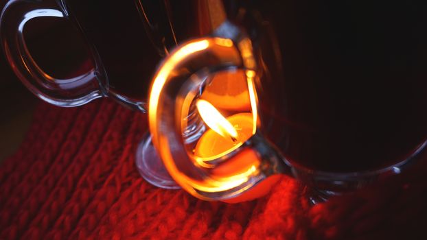 Mulled wine in glass mugs, burning candle on a dark red background. Red Hot wine with orange and red scarf