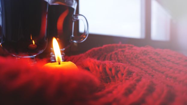 Mulled wine in glass mugs, burning candle on a dark red background. Red Hot wine with orange and red scarf