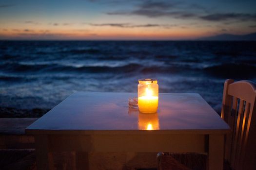 romantic table with burning candle by the sea at night
