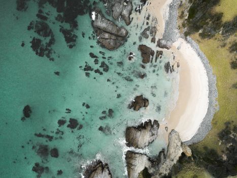 Aerial views of small arching beach dotted with large and small rocks with pristine aqua blue waqters.  The beaches here are idyllic hard to access and rip dominated.