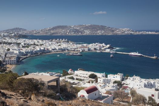 panoramic view of the Mykonos town harbor with famous windmills from the above hills on a sunny summer day, Mykonos, Cyclades, Greece 