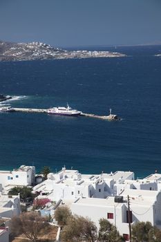 panoramic view of the Mykonos town harbor with famous windmills from the above hills on a sunny summer day, Mykonos, Cyclades, Greece 
