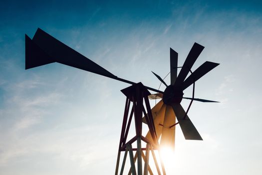 Silhouette of a backlit steel windpump at sunset, sun and sky in the background