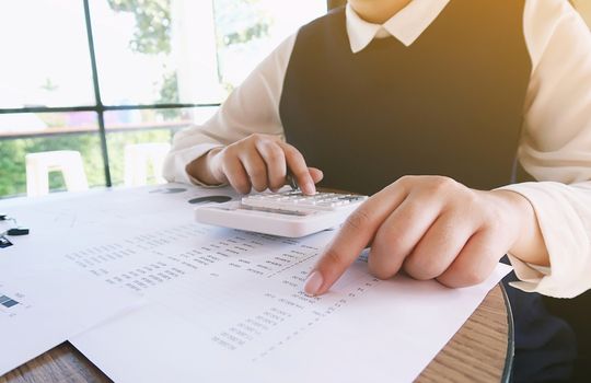 Businesswoman analyzing investment charts and pressing calculator buttons over documents. Accounting Concept