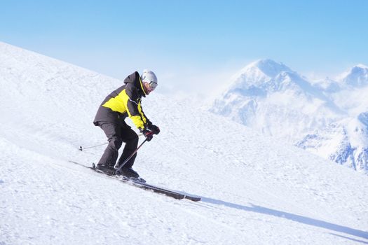 Alpine skier on piste running downhill in beautiful Alpine landscape. Blue sky on background. Free copy space for text