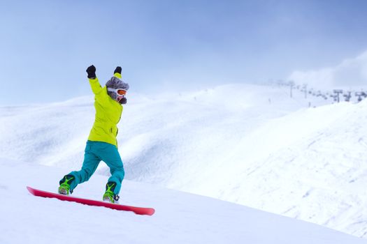 Girl snowboarder running down the slope in Alpine mountains. Winter sport and recreation, leisure outdoor activities. Image of excited screaming young woman enjoyment concept