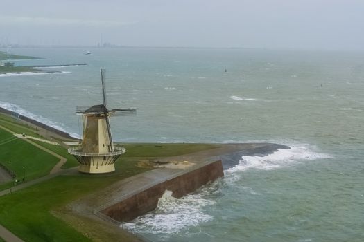 Windmill at the quay of Vlissingen with wild sea, typical dutch city in zeeland, the Netherlands