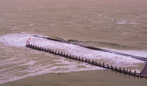 The pier jetty of vlissingen with wooden poles and small lighthouse, wild sea with waves at high tide, Zeeland, The Netherlands