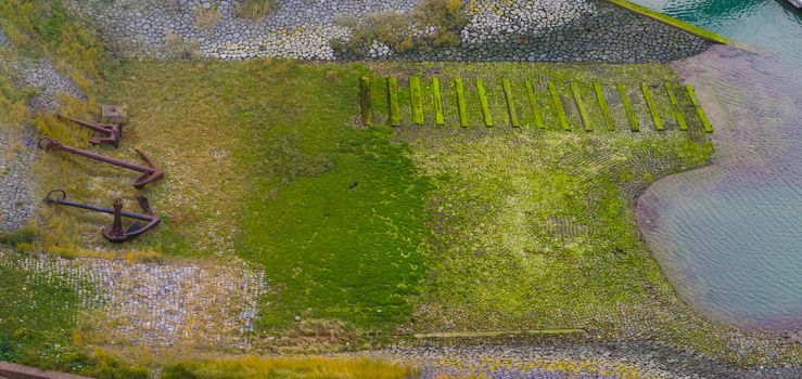 aerial shot of the harbor embankment of Vlissingen, stones covered in green seaweed with ship anchor decorations, dutch landscape