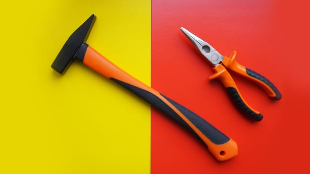 Tools worker, hammer, pliers on bright yellow and red background, top view. Repair tools