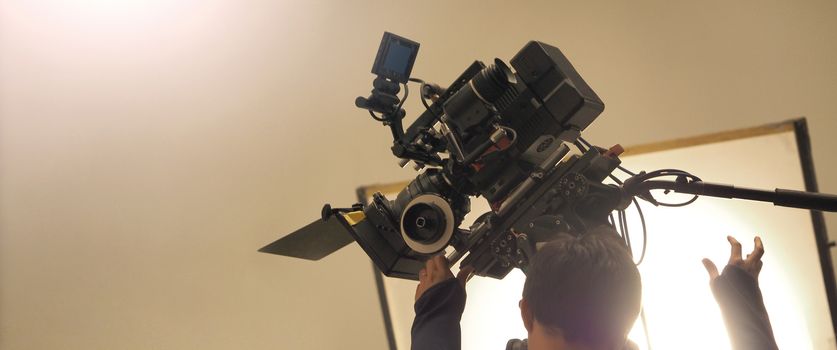 Behind the shooting or filming video movie and film production crew team setting up camera on tripod and professional equipment in studio for offline tv commercial or online web film recording.