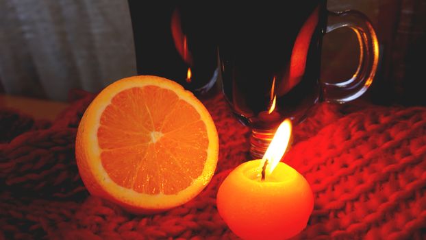 Mulled wine in glass mugs, burning candle on a dark red background. Red Hot wine with orange and red scarf