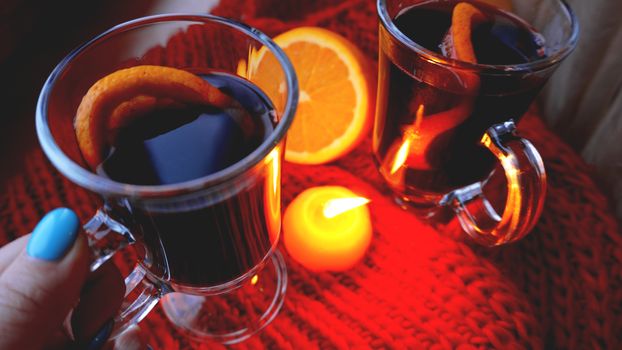 Mulled wine in glass mugs, burning candle on a dark red background. Red Hot wine with orange and red scarf