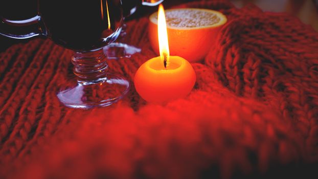 Mulled wine in glass mugs, burning candle on a dark red background. Red Hot wine with orange and red scarf