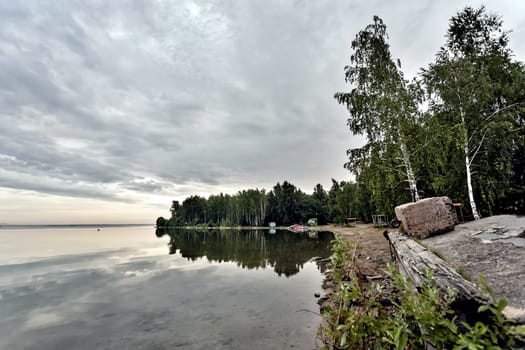 early morning on a calm lake in cloudy weather, water reflects clouds, no wind, silence