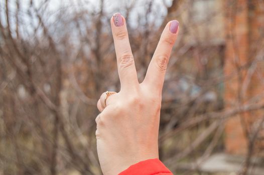 Female hand showing victory sign on blurred nature background.