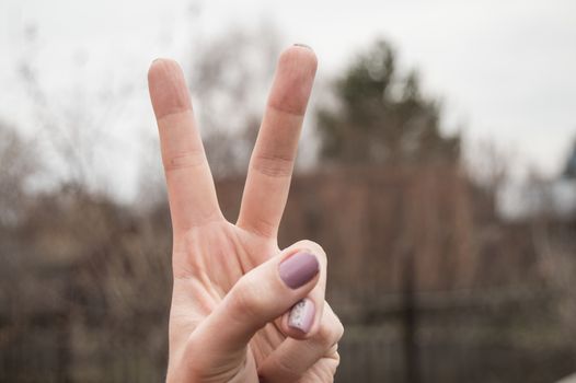 Female hand showing victory sign on blurred nature background.