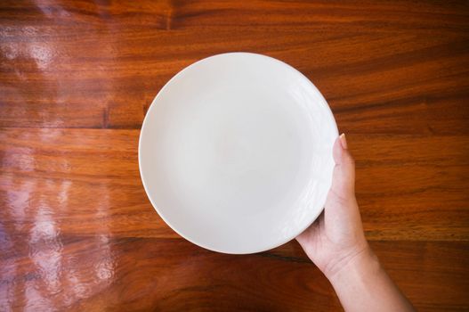 Female (woman) hands hold (support) a white dish (plate) on wooden table