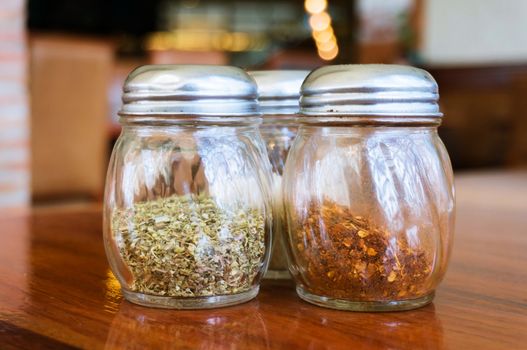 Glass of cheese salt and pepper shakers on wooden table in restaurant.