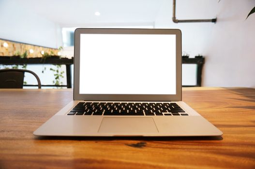 Laptop with Mock up blank screen on wooden table in front of coffeeshop cafe space for text. product display montage- technology concept.