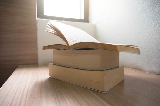 Open old books on a wooden table with window light.