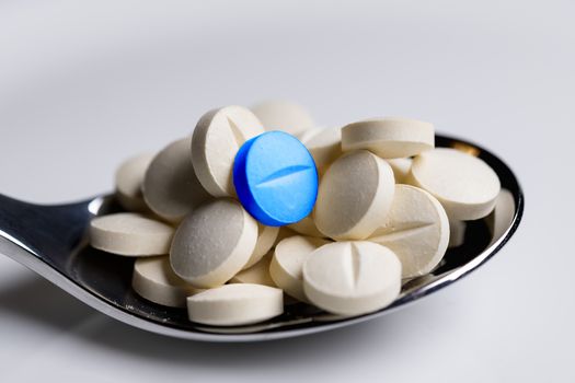 Close up of white tablets with one blue on a spoon on a table