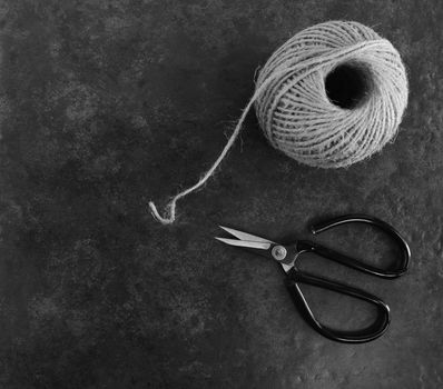 Ball of twine with traditional flower scissors on dark grey background with copy space - monochrome processing