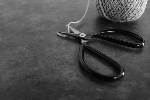 Old-fashioned scissors cutting piece of garden twine on grey background with copy space - monochrome processing