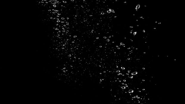 Close-up macro images of soda water bubbles floating up to top of water surface which little and big circle texture splashing up by gas power in carbonate drink make refreshing moment on black background.