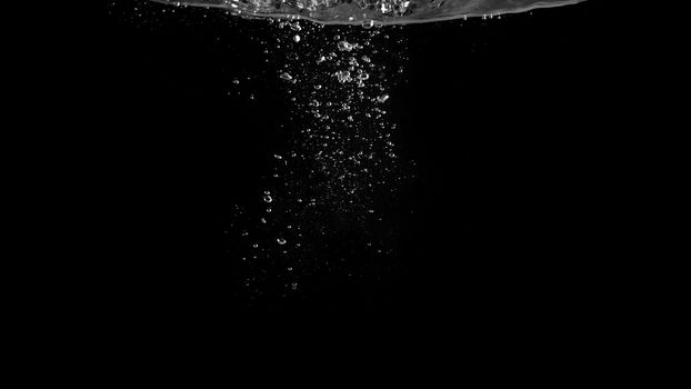 Close-up macro images of soda water bubbles floating up to top of water surface which little and big circle texture splashing up by gas power in carbonate drink make refreshing moment on black background.