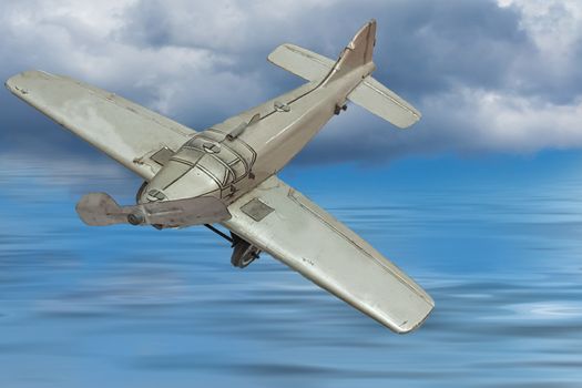 Picture of a retro gray metal toy airplane. In the background, blue sky with clouds and sea.