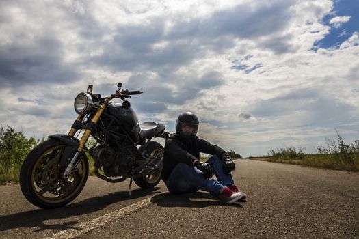 man with helmet sitting near the motorcycle in the road