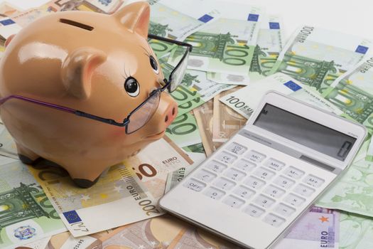 Piggy Bank on Euro Banknotes With White Calculator. European Health Insurance Costs