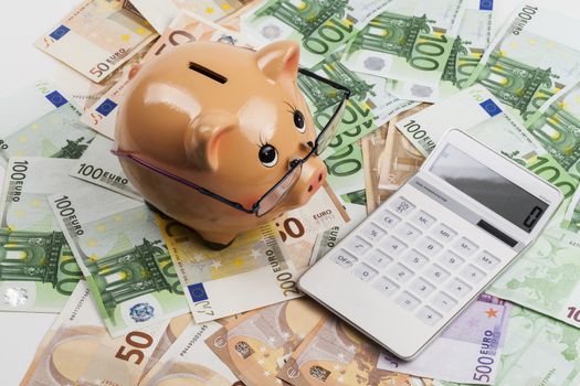 Piggy Bank on Euro Banknotes With White Calculator. European Health Insurance Costs