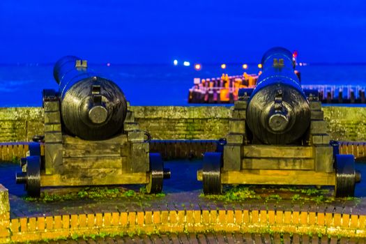 closeup of two pirate cannons, the pier jetty and sea of vlissingen in the background