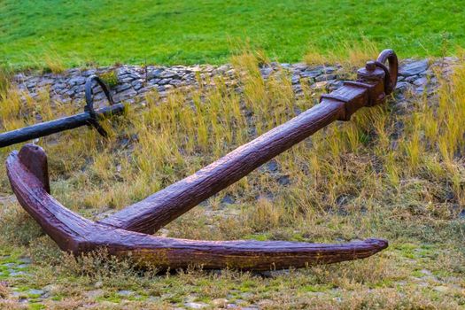 Big old rusty pirate ship anchor laying on the ground, harbor decoration background