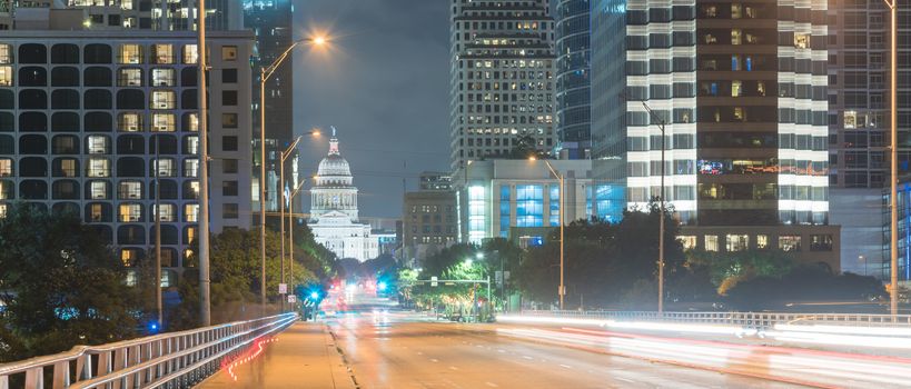 Panorama view downtown Austin at night with traffic light trail lead to Texas State capitol building. View from pedestrian sidewalk on bridge across Colorado River