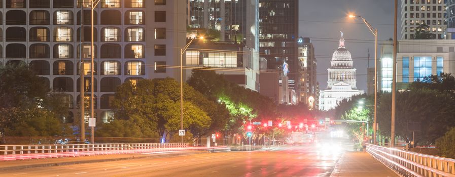 Panorama view downtown Austin at night with traffic light trail lead to Texas State capitol building. View from pedestrian sidewalk on bridge across Colorado River