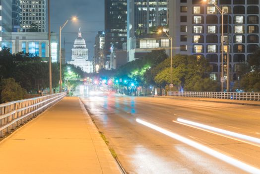 Downtown Austin at night with traffic light trail lead to Texas State capitol building. View from pedestrian sidewalk on bridge across Colorado River