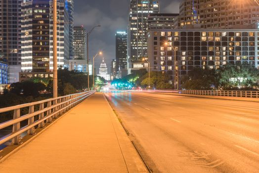 Downtown Austin at night with traffic light trail lead to Texas State capitol building. View from pedestrian sidewalk on bridge across Colorado River