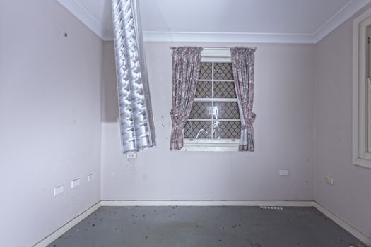 Empty room or office of old abandoned building.  The cover of the fluorescent light fitting is left dangling from the ceiling and the windows have been boarded up